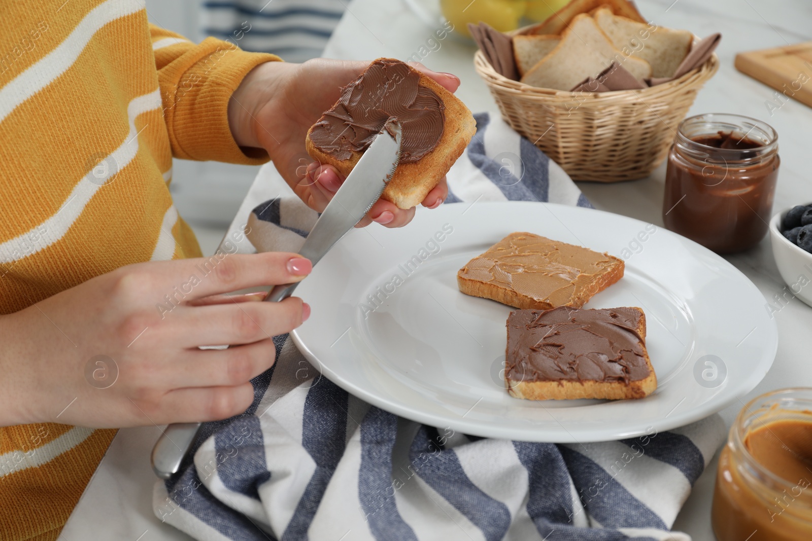 Photo of Woman spreading tasty nut butter onto toast at table, closeup