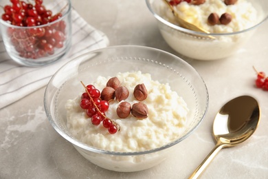 Photo of Creamy rice pudding with red currant and hazelnuts in bowls served on grey table