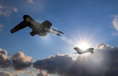Image of Silhouettes of jet fighters in cloudy sky on sunny day