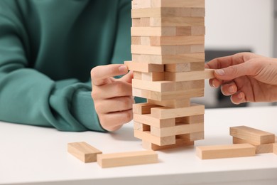 Photo of People playing Jenga tower at white table indoors, closeup