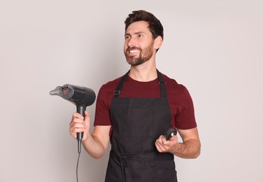 Smiling hairdresser with dryer and brush on light grey background