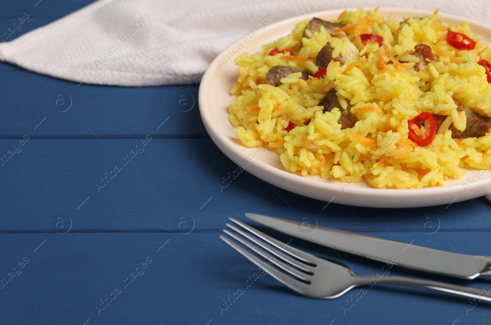 Photo of Delicious pilaf with meat served on blue wooden table, closeup. Space for text