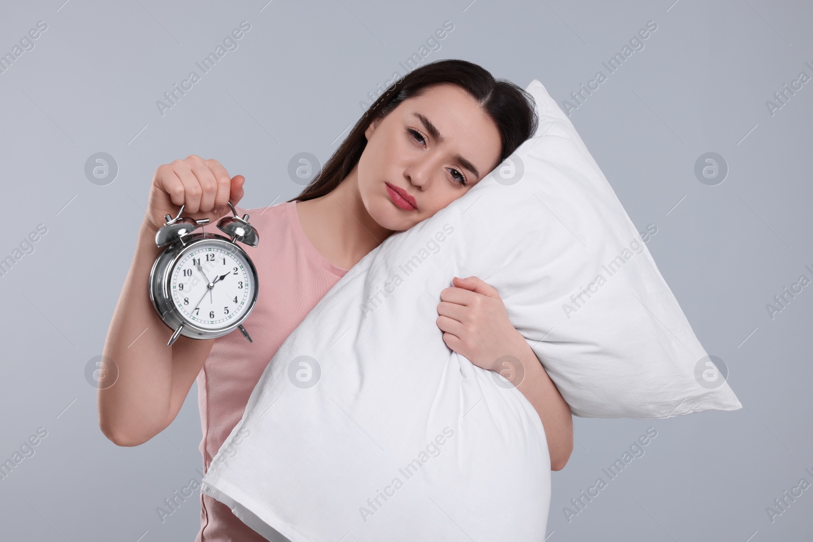 Photo of Tired young woman with pillow and alarm clock on light grey background. Insomnia problem