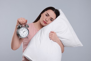 Tired young woman with pillow and alarm clock on light grey background. Insomnia problem