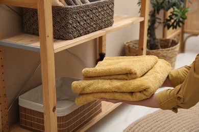 Photo of Woman putting towels into storage basket indoors, closeup