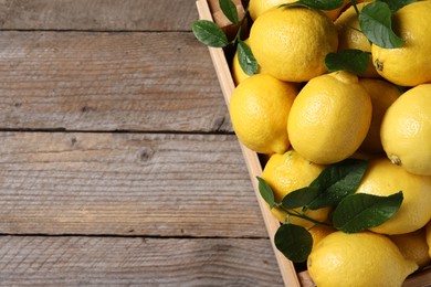 Fresh lemons and green leaves in crate on wooden table, top view. Space for text