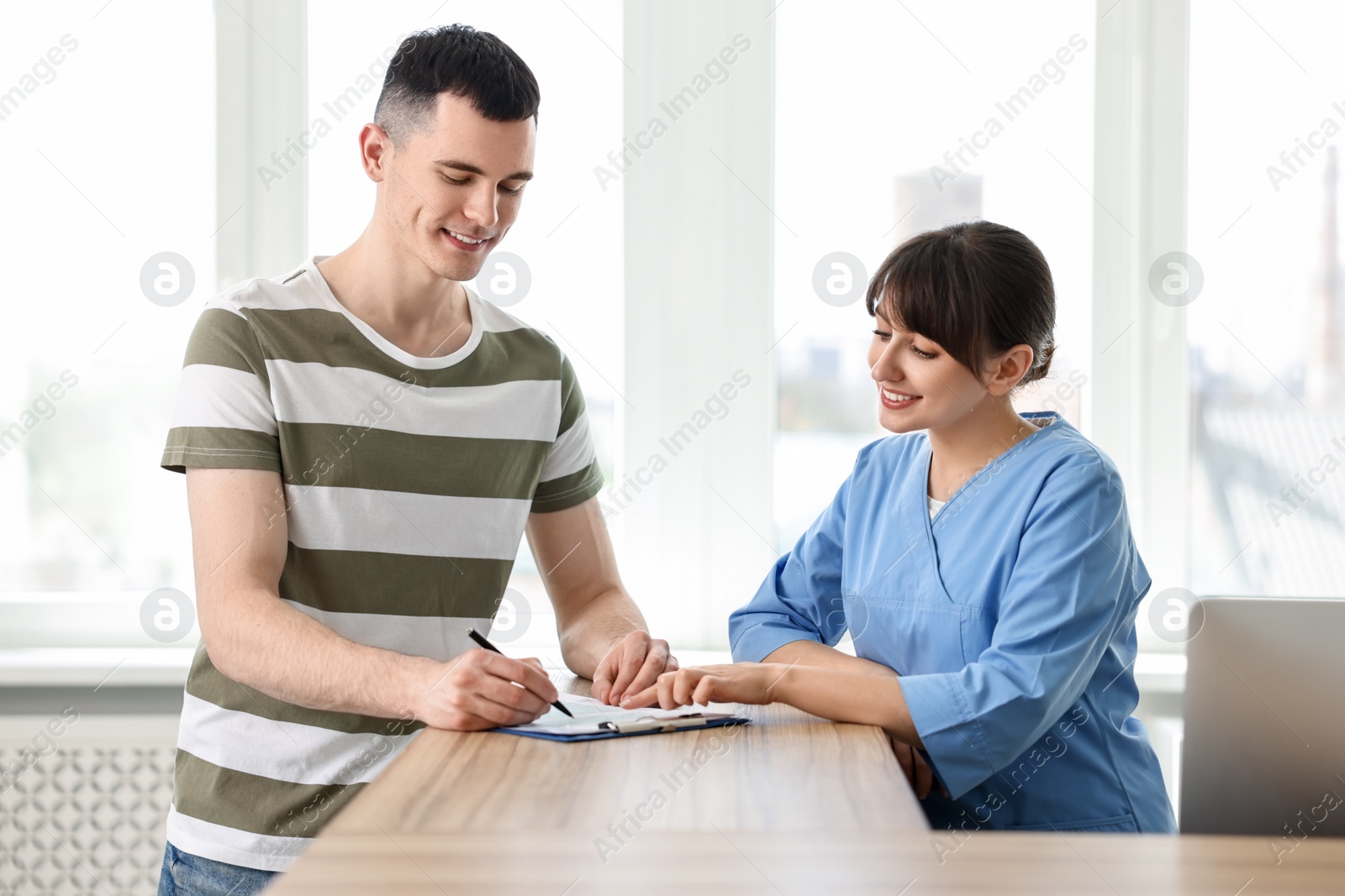 Photo of Smiling medical assistant working with patient at hospital reception