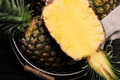 Photo of Whole and cut ripe pineapples in metal basket on black table, top view