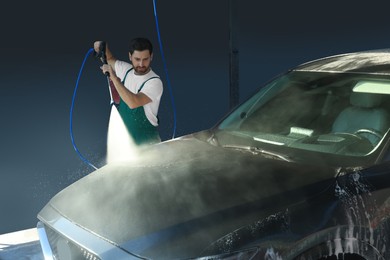 Worker washing auto with high pressure water jet at outdoor car wash