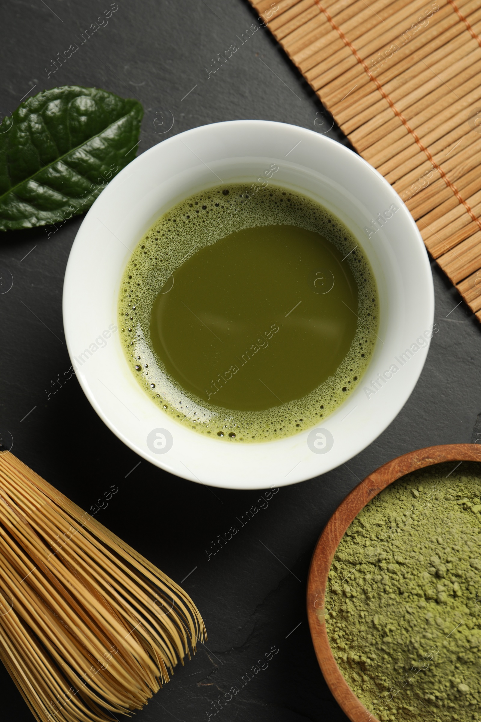 Photo of Fresh matcha tea, green powder and bamboo whisk on black table, flat lay