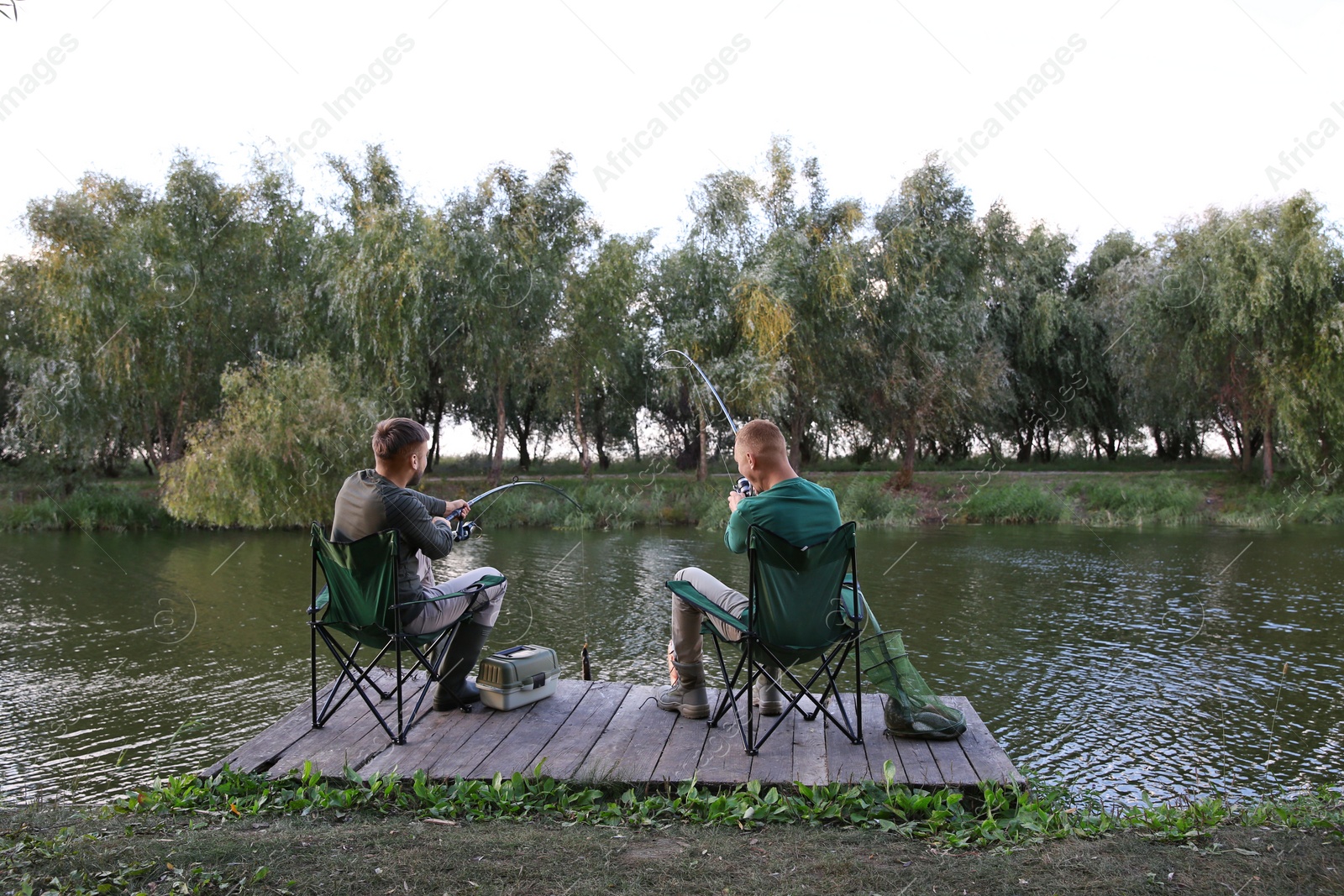 Photo of Friends fishing on wooden pier at riverside. Recreational activity