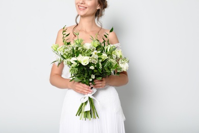 Young bride wearing wedding dress with beautiful bouquet on light grey background, closeup