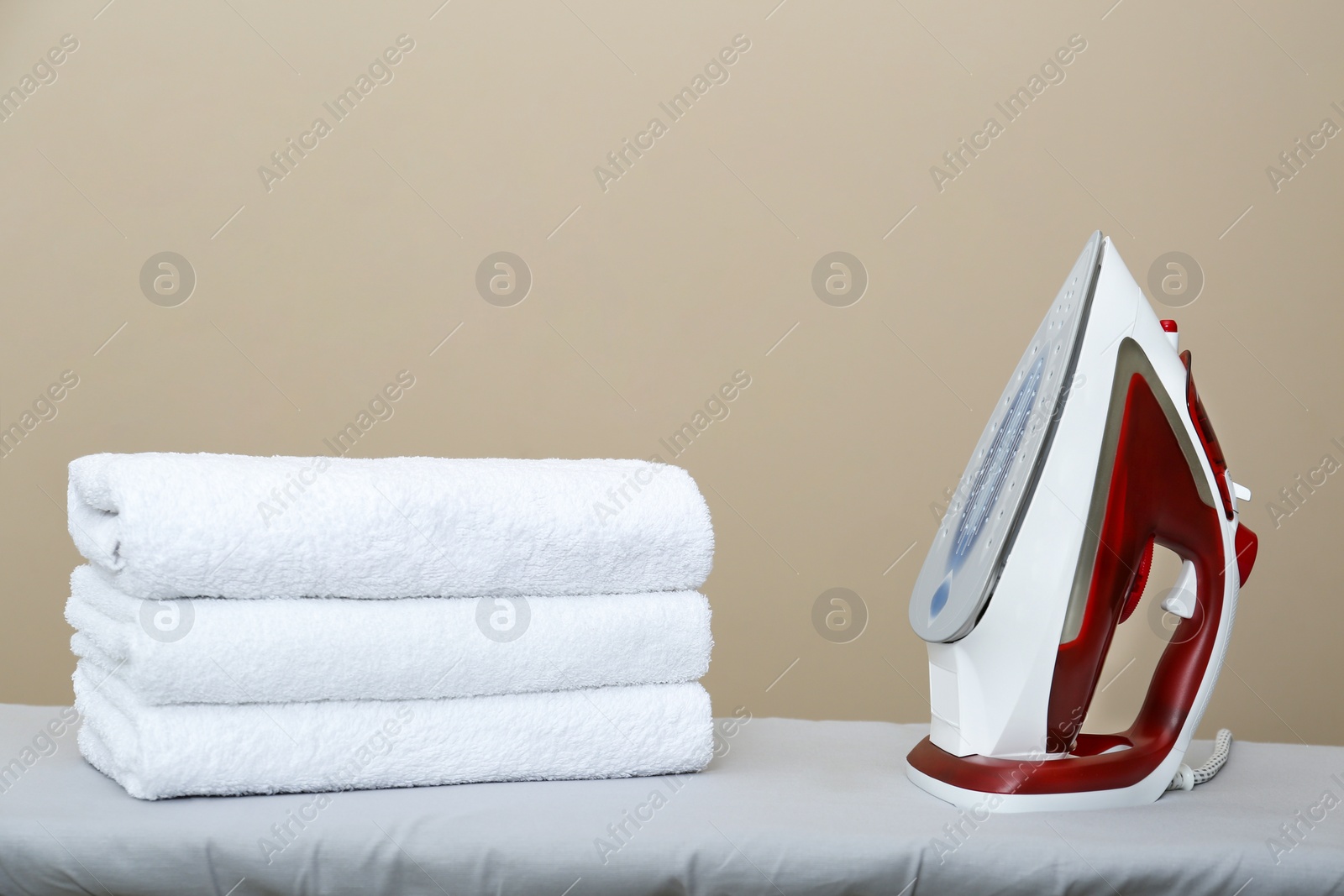 Photo of Modern iron and clean towels on board against beige background