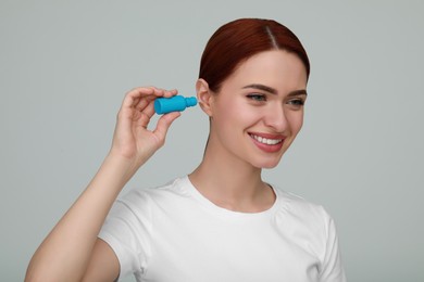 Photo of Woman using ear drops on light grey background
