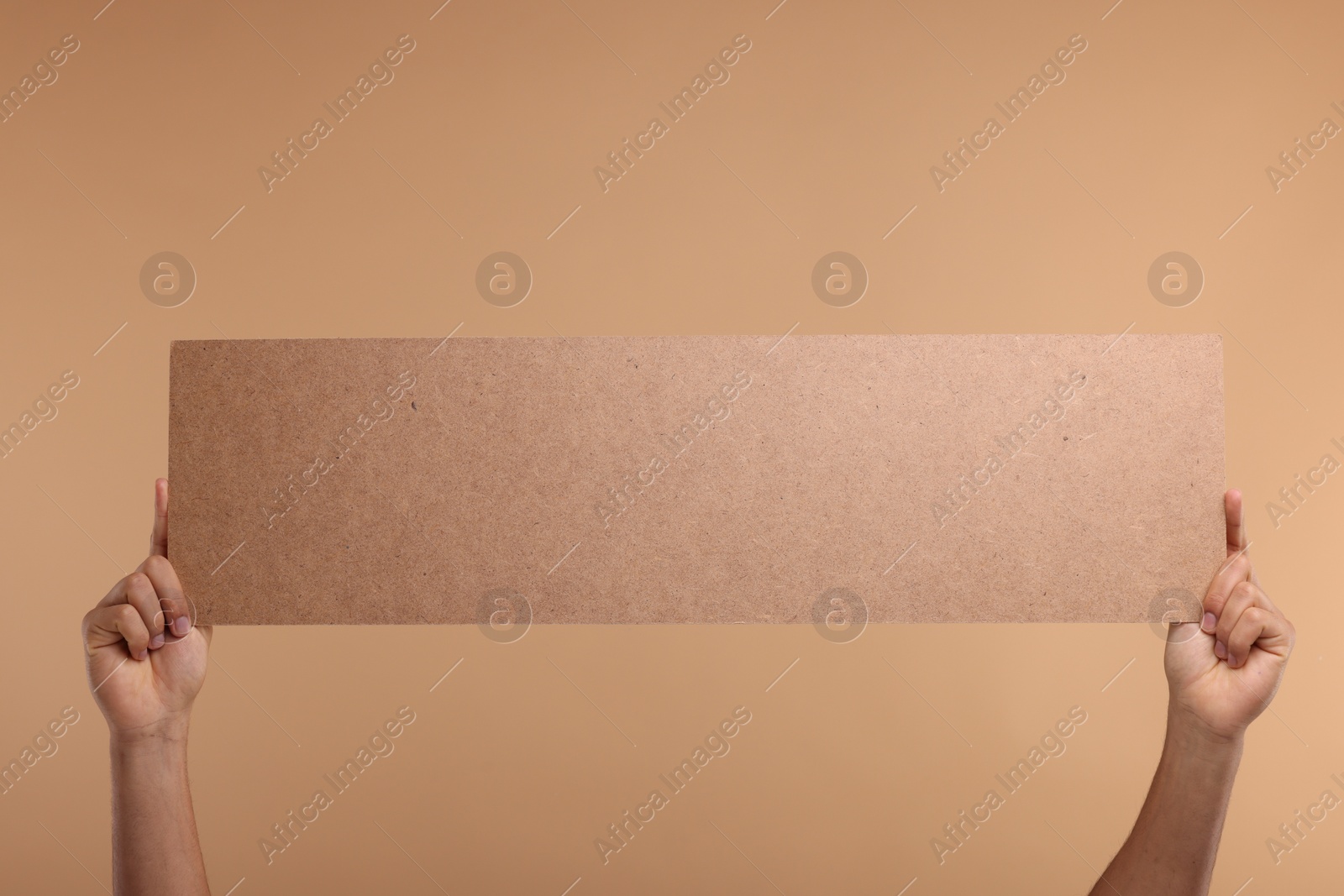 Photo of Man holding blank cardboard banner on beige background, closeup. Space for text