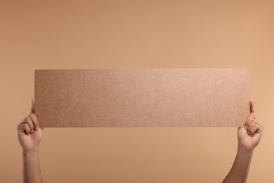 Man holding blank cardboard banner on beige background, closeup. Space for text