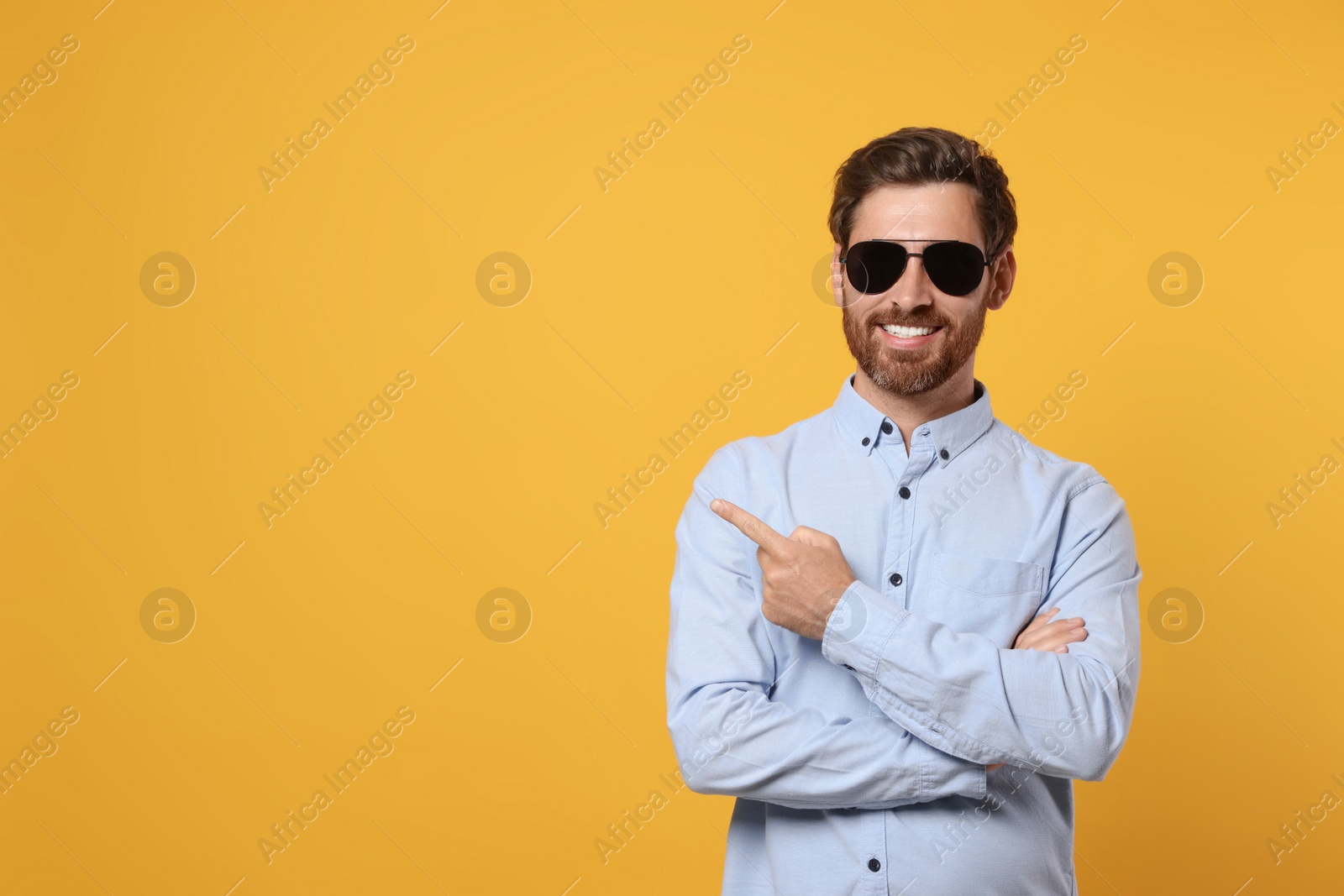 Photo of Portrait of smiling bearded man with stylish sunglasses on orange background. Space for text