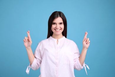 Photo of Happy young woman crossing fingers on light blue background. Dealing with stress