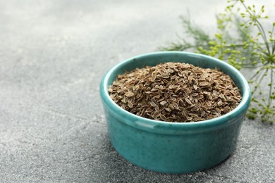 Photo of Bowl of dry seeds and fresh dill on grey table, closeup. Space for text