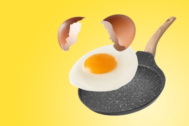 Image of Tasty fried chicken egg with shell falling into frying pan on yellow background