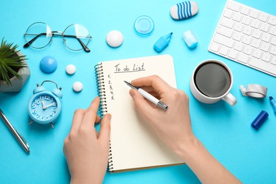 Woman filling To Do list in notepad at light blue table, top view