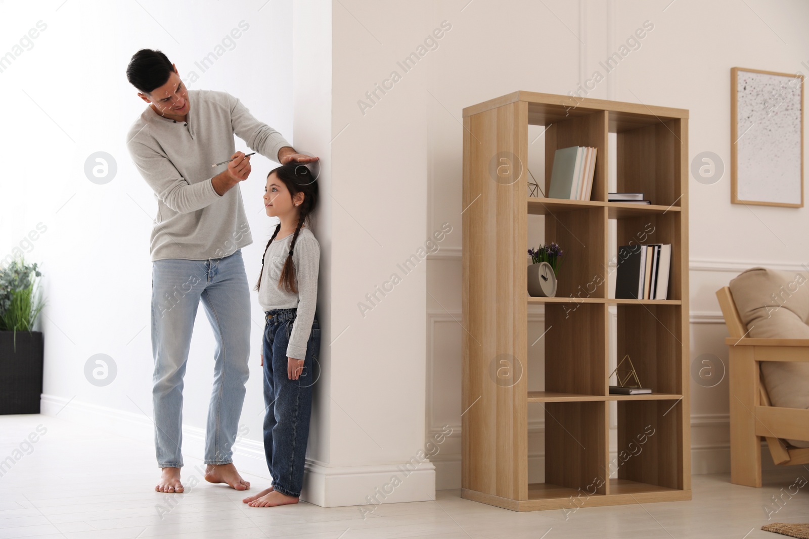 Photo of Father measuring height of his daughter near wall at home