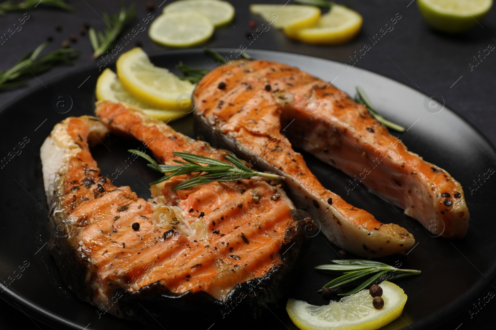 Photo of Plate with tasty salmon steaks on black table, closeup