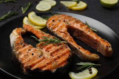 Photo of Plate with tasty salmon steaks on black table, closeup