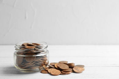 Photo of Glass jar and coins on table against light background. Space for text