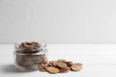 Glass jar and coins on table against light background. Space for text