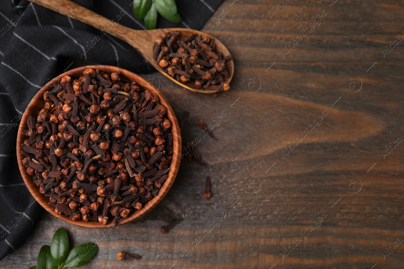 Photo of Bowl and spoon with aromatic cloves on wooden table, flat lay. Space for text