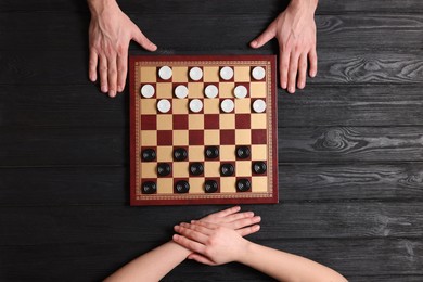 Man playing checkers with woman at black wooden table, top view
