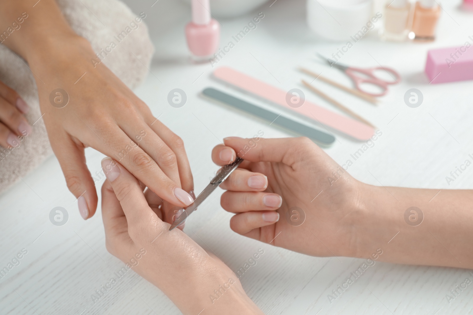 Photo of Manicurist filing client's nails at table, closeup. Spa treatment