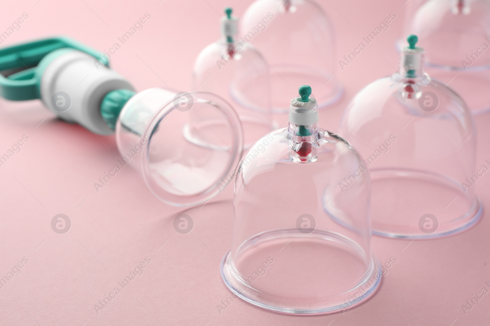 Photo of Plastic cups and hand pump on pink background, closeup. Cupping therapy