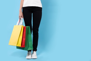 Woman with shopping bags on light blue background, closeup. Space for text