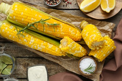 Tasty cooked corn cobs on wooden table, flat lay