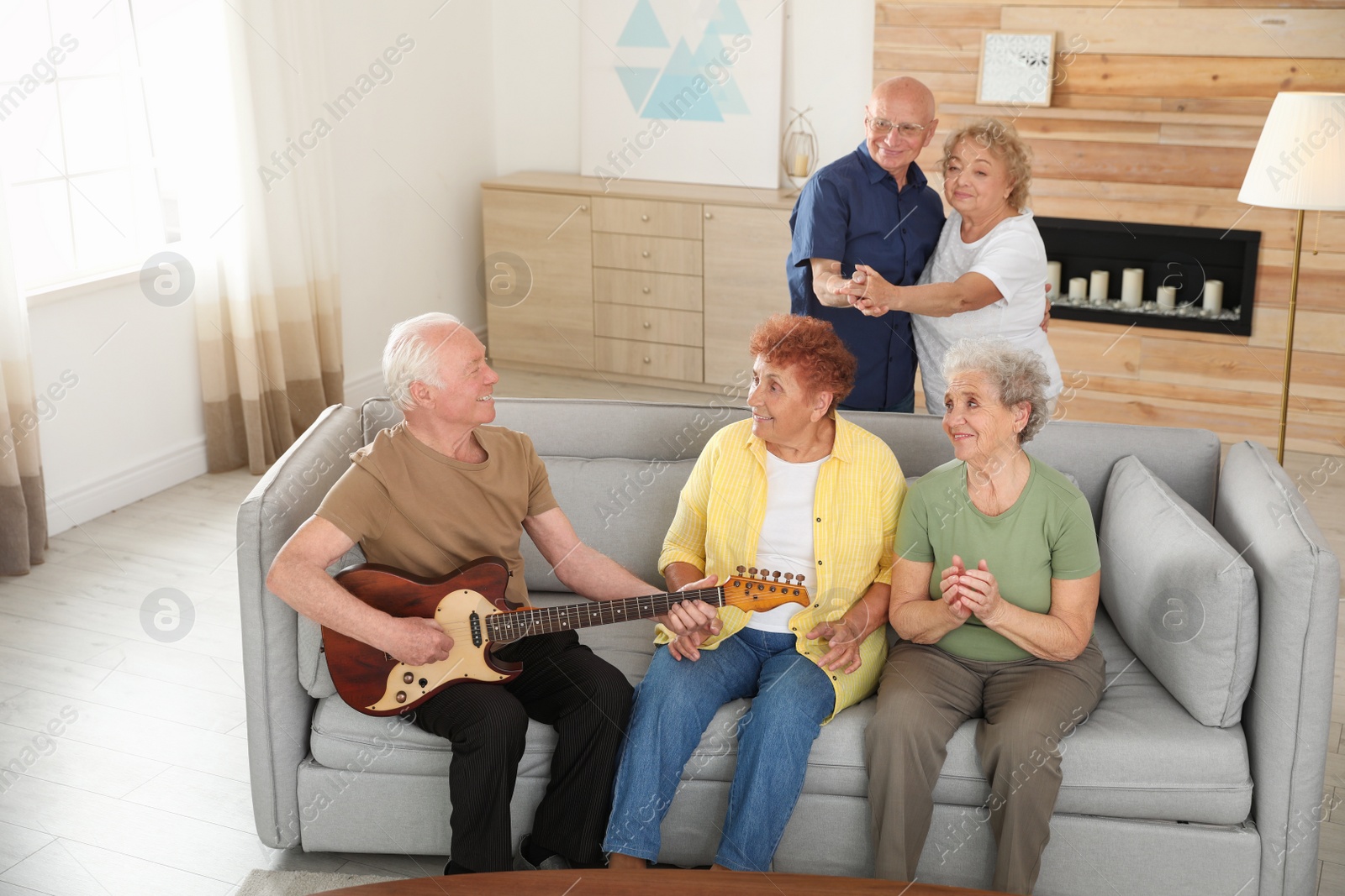 Photo of Elderly man playing guitar for his friends in living room