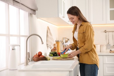 Young woman peeling zucchini at kitchen counter. Preparing vegetable