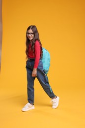 Cute schoolgirl in glasses on orange background