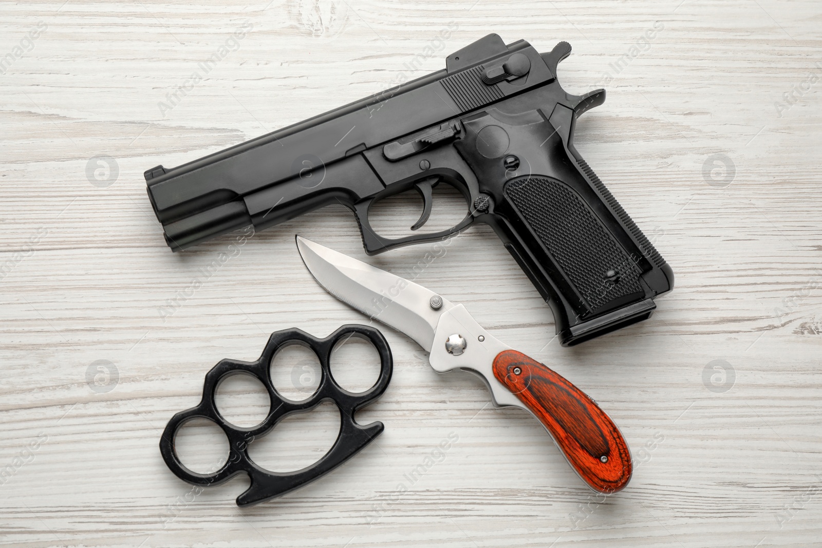 Photo of Black brass knuckles, gun and knife on white wooden background, flat lay