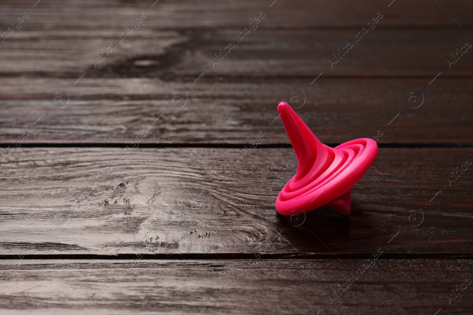 Photo of One pink spinning top on wooden table, closeup. Space for text