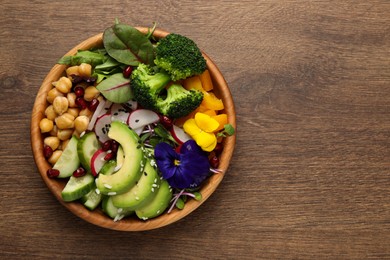 Delicious vegan bowl with broccoli, avocados and violet flowers on wooden table, top view. Space for text