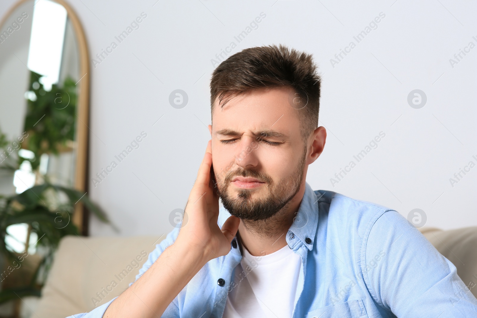 Photo of Young man suffering from ear pain at home. Space for text