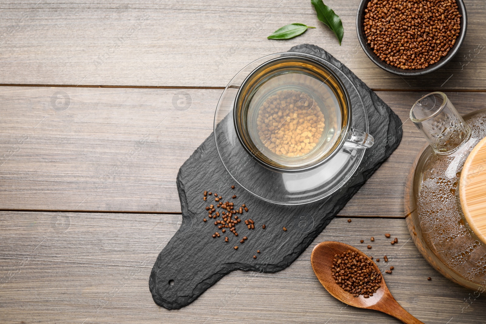 Photo of Cup of freshly made aromatic buckwheat tea and granules on wooden table, flat lay. Space for text