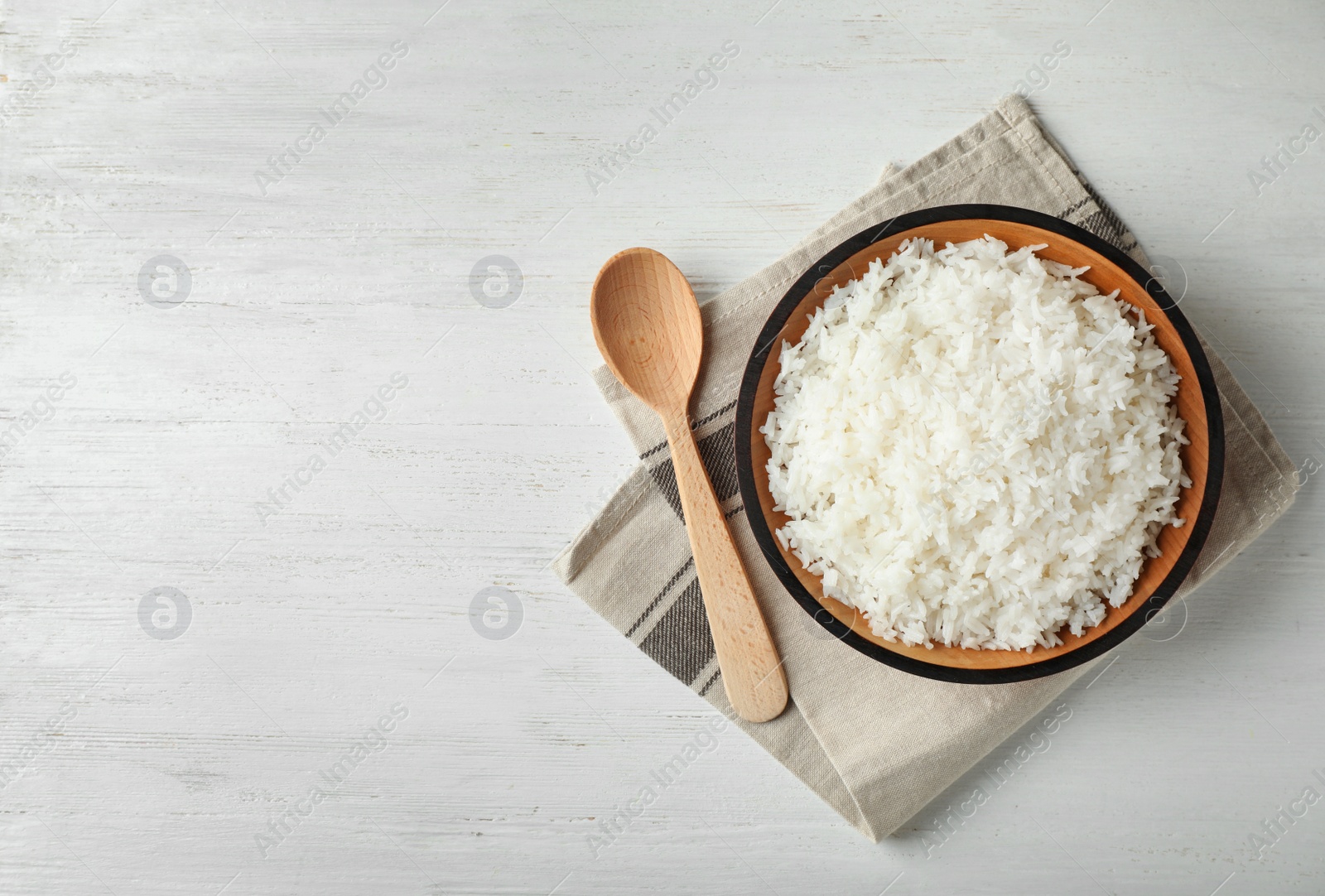 Photo of Bowl of boiled rice and spoon on wooden background, top view with space for text