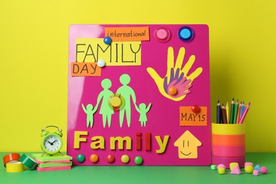Photo of Happy International Family Day. Composition with stationery on green table against yellow background