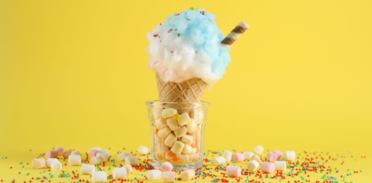 Sweet cotton candy in waffle cone on yellow background, closeup