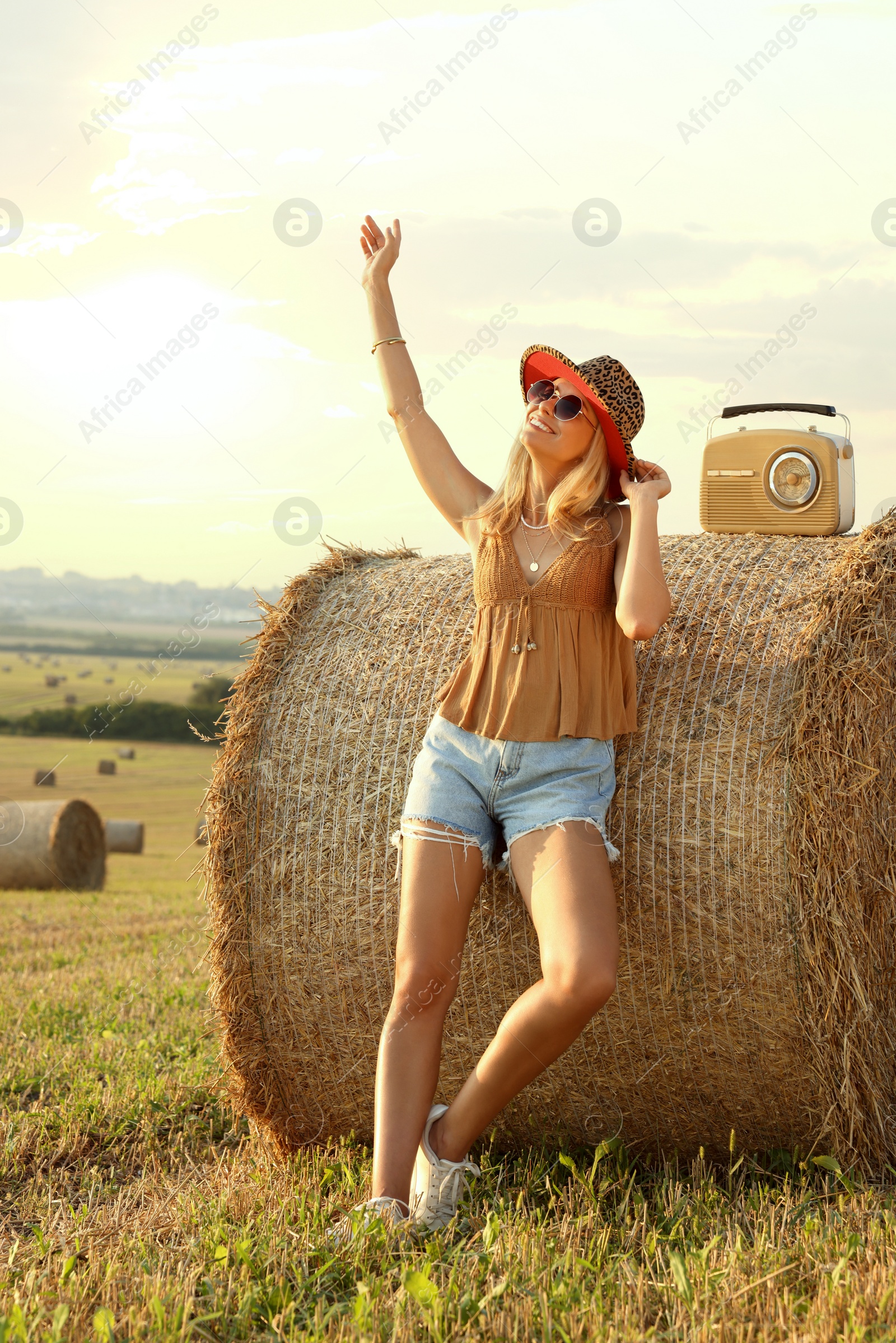 Photo of Happy hippie woman with receiver near hay bale in field