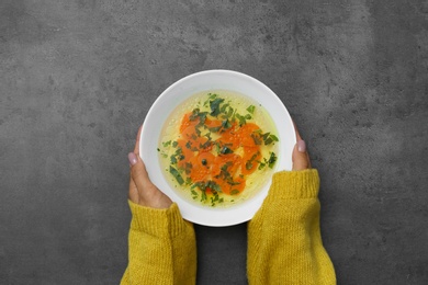 Photo of Woman with bowl of soup at grey table, top view. Flu treatment