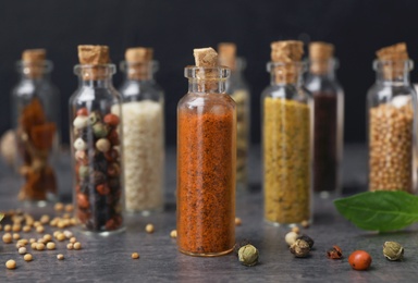 Glass bottles with different spices on table against dark background, closeup